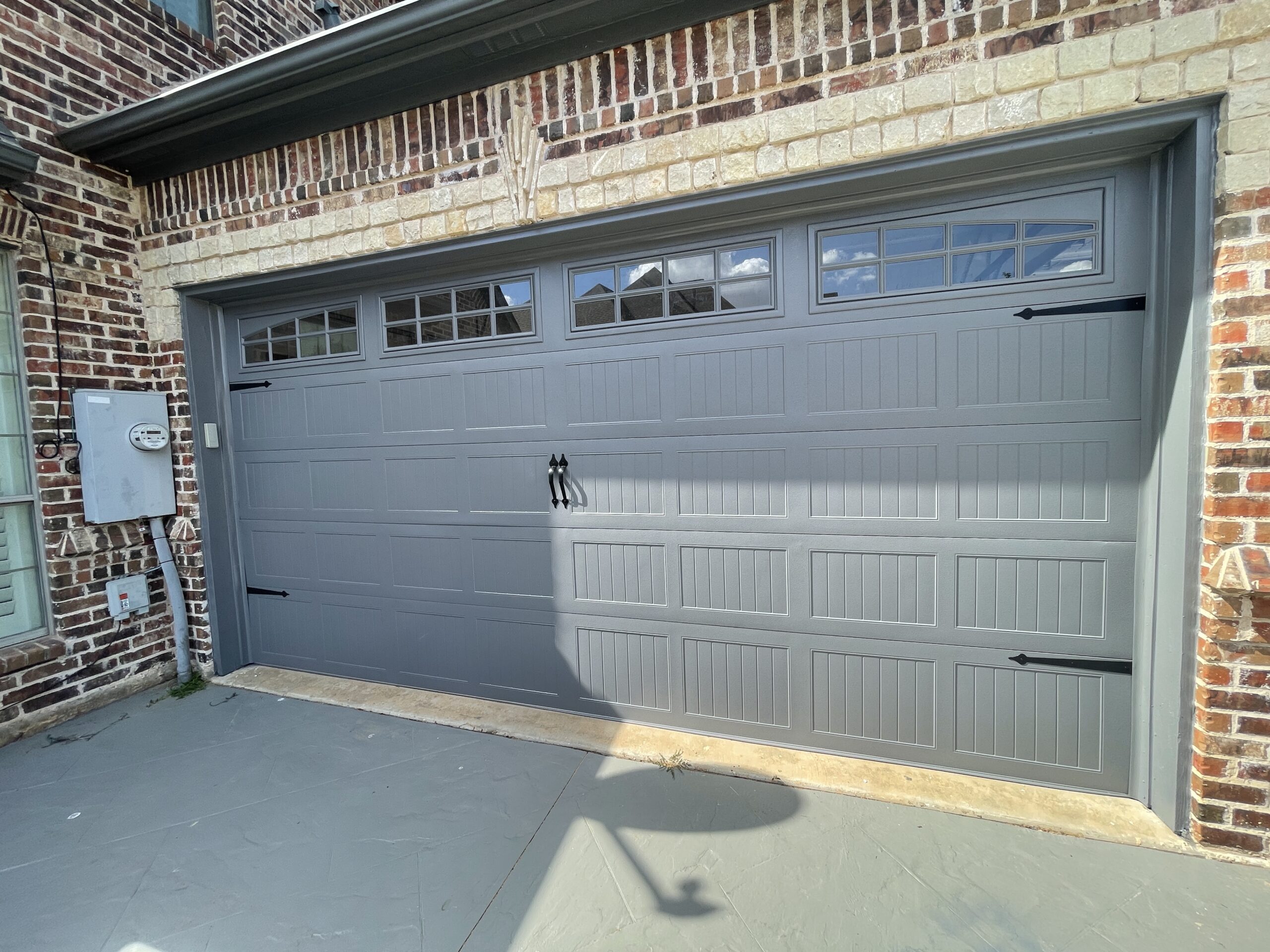 Grey carriage style residential garage door with windows.