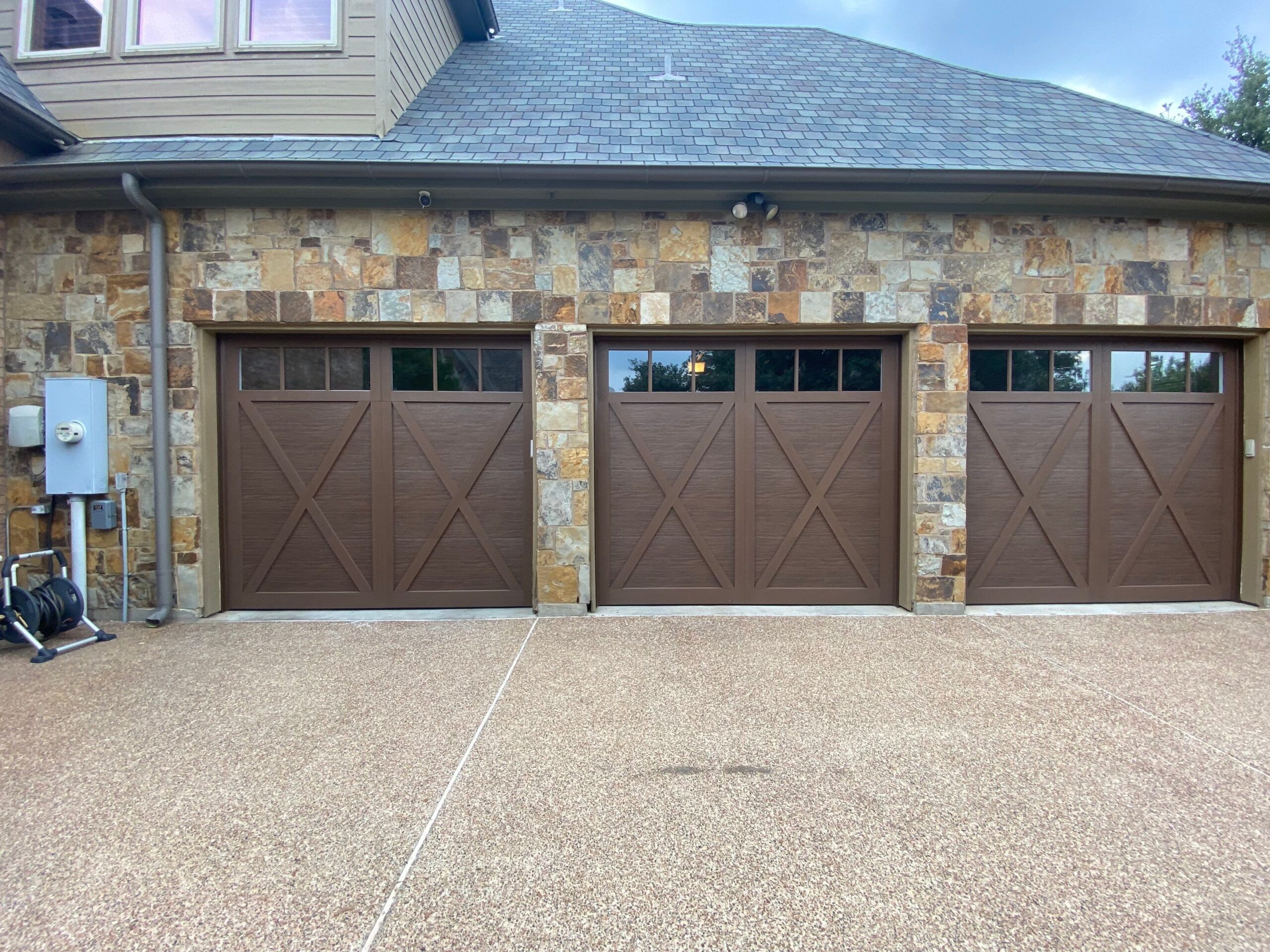 Three single car garage doors. Brown, carriage style, with wood texturing, and windows.